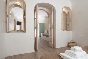A hotel room with a wooden floor, a bed, a TV, and a bathroom visible through an open door. - White Orchid Cave House & Studio (Santorini)