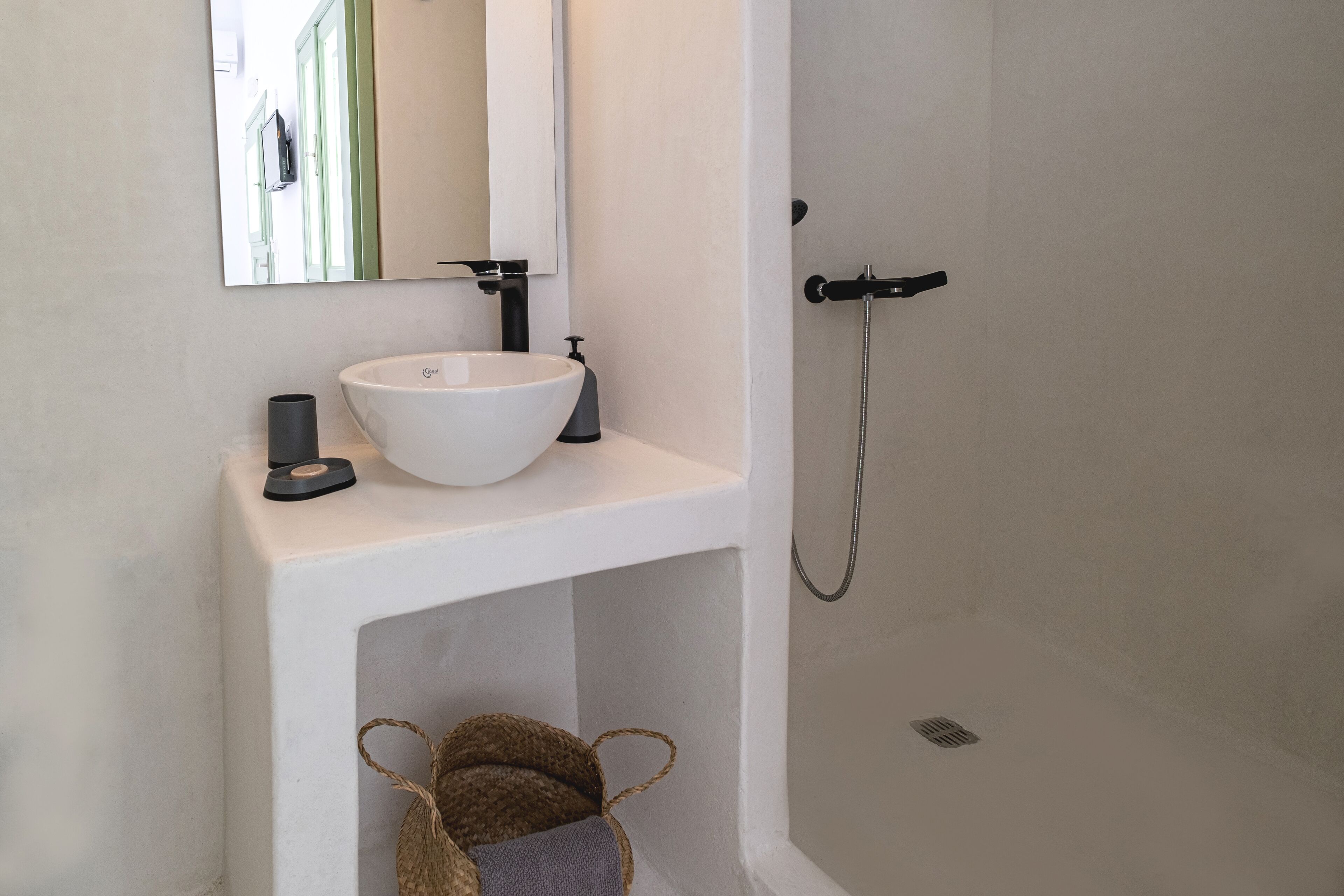 Un bagno con un lavandino bianco, uno specchio, un soffione a mano e un piccolo cesto.