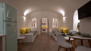 Une cuisine moderne agrémentée d’un réfrigérateur au style rétro, un coin repas avec une table dressée pour deux personnes et un espace salon confortable avec des coussins.