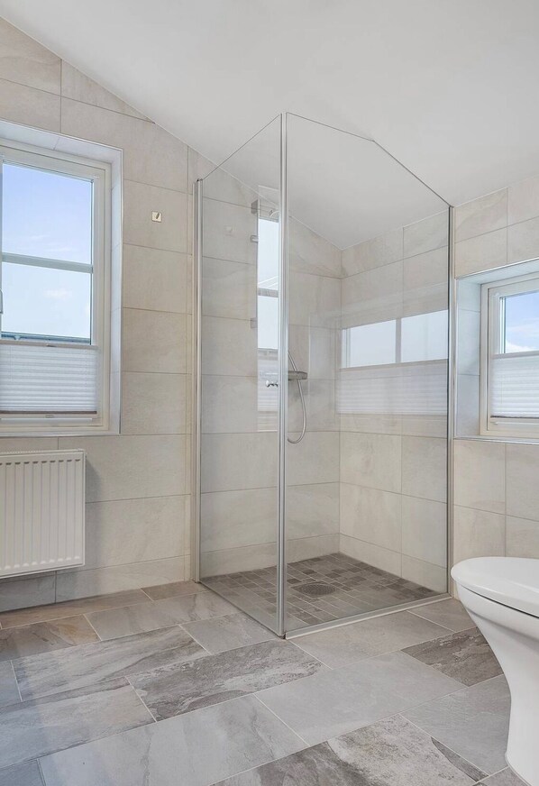 A modern bathroom with a glass shower enclosure, a toilet, and a window providing natural light.