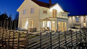 Ein zweistöckiges Haus mit Balkon, überdachter Terrasse und Auffahrt mit geparkten Autos.