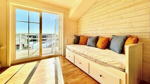 Ein Zimmer mit einer großen Schiebeglasdoor, die auf einen Balkon führt, einer Holzbalkendecke, einem Sofa mit vielen Kissen und einem kleinen Tisch.