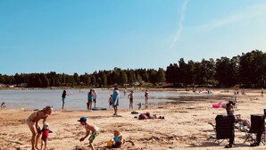 Eine Strandansicht mit Menschen, darunter spielenden Kindern im Sand, sowie einigen Liegestühlen und Sonnenschirmen.