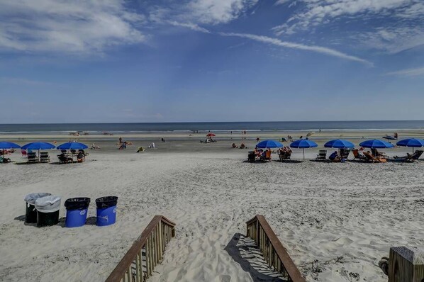 Une plage avec des parasols bleus, une promenade en bois et des poubelles.