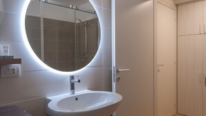 Un bagno con uno specchio rotondo, un lavandino e una cabina doccia.