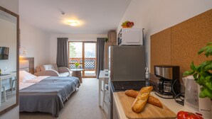 A hotel room with a bed, a desk, a dining area, a kitchen with a microwave, a coffee maker, and a cutting board with bread. - RentPlanet - Apartamenty Okrzei (Szklarska Poreba)