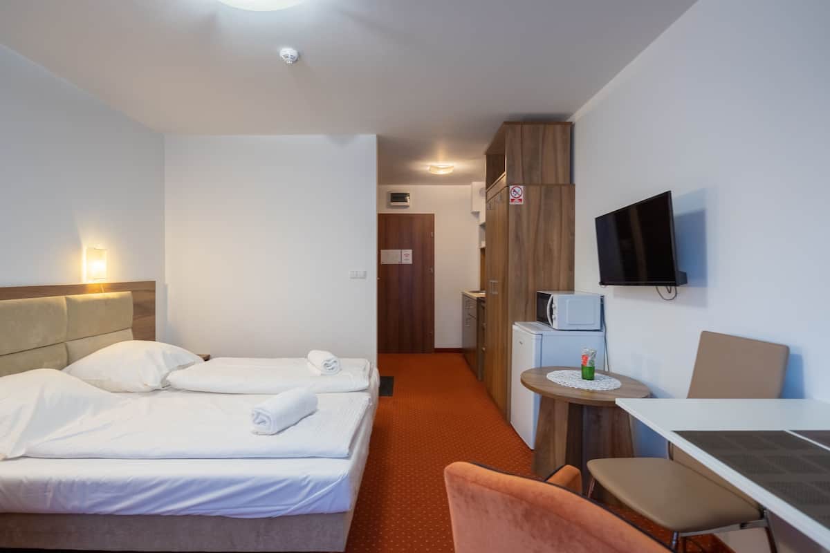 A hotel room with a bed, a desk, a chair, a television, and a kitchenette.
