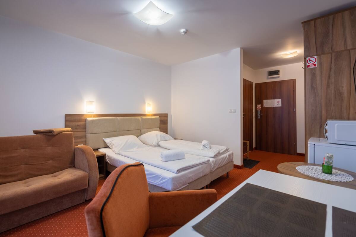 A hotel room with two single beds, a sofa, a chair, a small table, and a microwave.