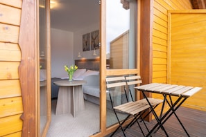 A wooden deck with a table and chairs, a small round table with a vase of flowers, and a bed with a headboard in the background. - RentPlanet - Apartamenty Okrzei (Szklarska Poreba)