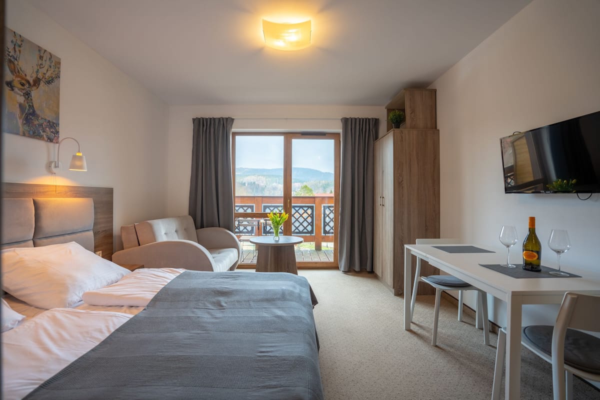 A hotel room with a bed, a desk, a chair, a television, and a balcony with curtains.
