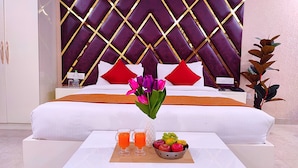 Ein Hotelzimmer mit einem großen Bett, einem Nachttisch mit Telefon, einer Vase mit Blumen, zwei Gläsern Orangensaft und einer Obstschale.