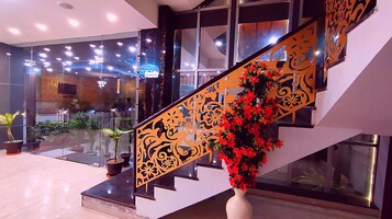 A modern interior with a glass staircase, a decorative railing, and a potted plant with red flowers.
