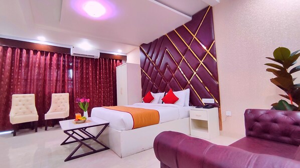 A hotel room with a bed, two chairs, a small table, a nightstand, and a potted plant. - Hotel Aradhna Inn by ShriGo Hotels (Bakshi Ka Talab)