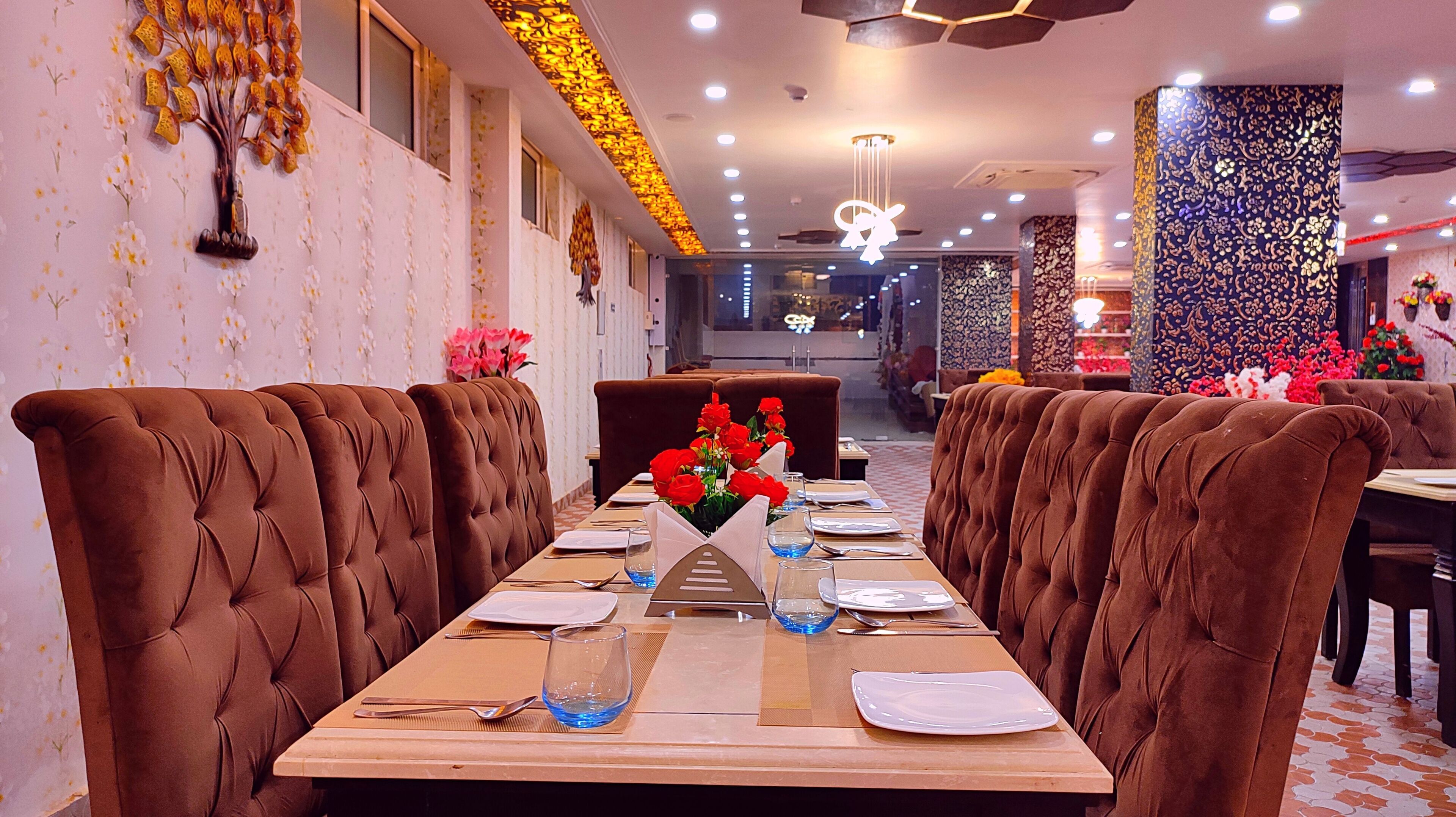 Un restaurant avec une longue table dressée pour le dîner, agrémentée de chaises à revêtement marron et d’un centre de table composé de fleurs rouges.