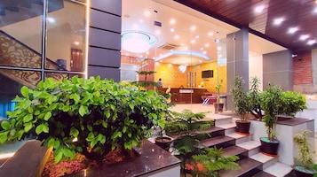 A reception area with a modern design, including a reception desk, seating area, and a staircase with potted plants.