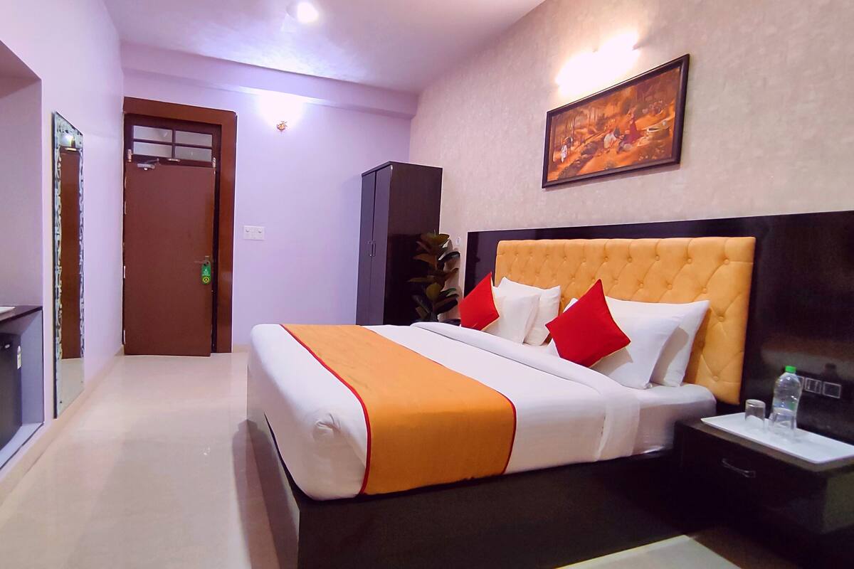 Ein Hotelzimmer mit Bett, Nachttisch, Schreibtisch mit Computer, Tür und einem Bild an der Wand.