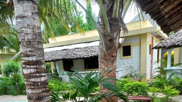 A tropical garden with palm trees, a swimming pool, and a building with a thatched roof. - Stay. Plus Darad Homes Diani (Ukunda)