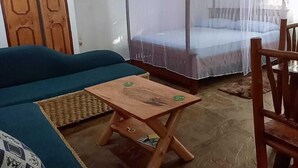 A room with a bed under a mosquito net, a sofa, a wooden table, and a chair. - Stay. Plus Darad Homes Diani (Ukunda)