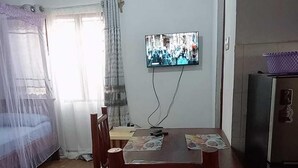 A room with a bed, a dining table with chairs, a television mounted on the wall, and a refrigerator. - Stay. Plus Darad Homes Diani (Ukunda)