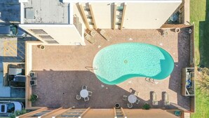 An aerial view of a rooftop pool area with a swimming pool, sun loungers, and a covered seating area.