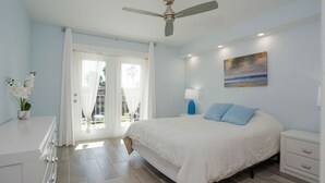 A bedroom with a bed, a nightstand, a lamp, a ceiling fan, and a painting on the wall.