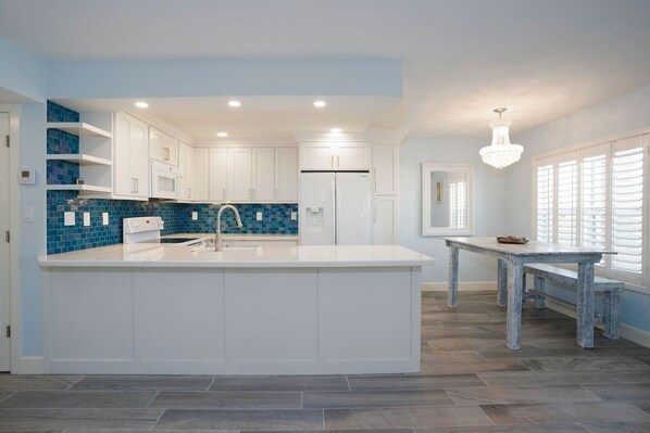 A modern kitchen with white cabinetry, a blue tiled backsplash, and a central island.