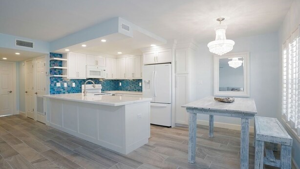 A modern kitchen with white cabinetry, a blue backsplash, and a central island.