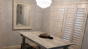 A dining area with a rustic wooden table, two barstools, a chandelier, and a large mirror on the wall.