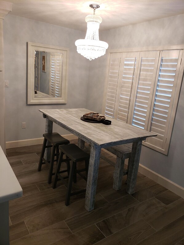 A dining area with a rustic wooden table, two barstools, a chandelier, and a large mirror on the wall.