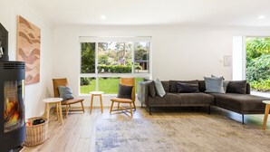 A modern living room with a large window, a fireplace, a sofa, and a coffee table. - Coastal Oasis - Pet Friendly - 6 Mins Walk to Beach (Callala Beach)
