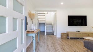 A modern living room with a staircase, a flat-screen TV, and a wooden bench. - Coastal Oasis - Pet Friendly - 6 Mins Walk to Beach (Callala Beach)