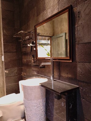A bathroom with a wooden wall, a sink, a mirror, and a shower area.