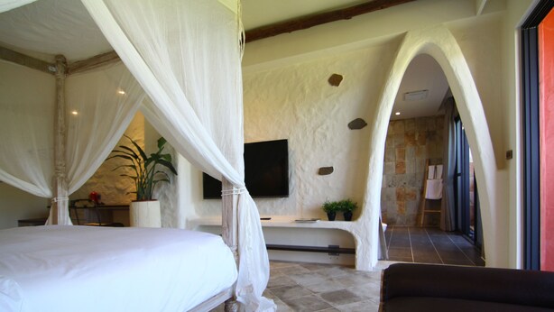 Un dormitorio con cama con dosel, televisor montado en la pared y pared de piedra con un arco.
