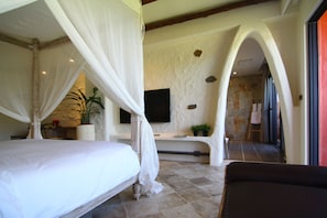 A bedroom with a four-poster bed, a television mounted on the wall, and a stone wall with an archway.