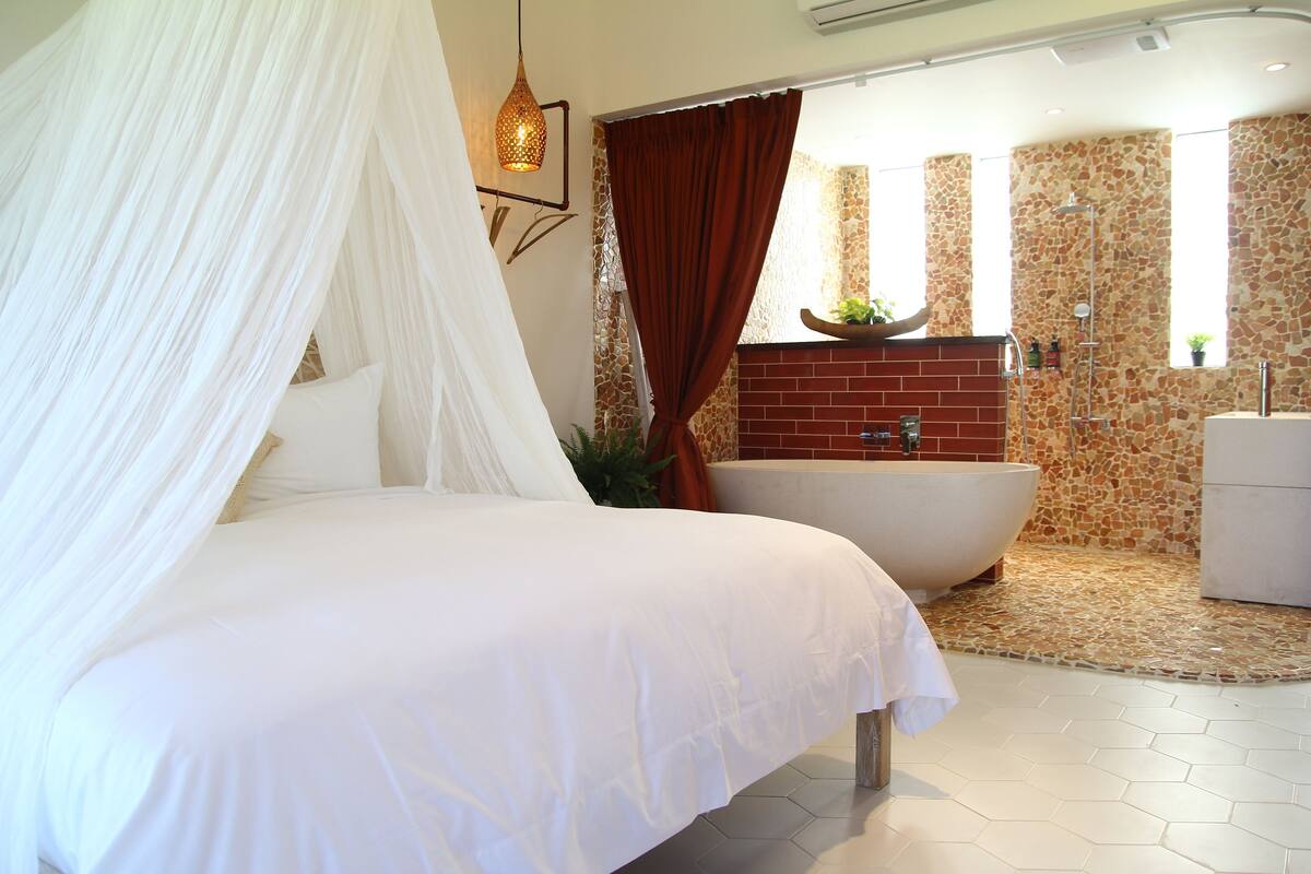 Ein Schlafzimmer mit Himmelsbett, einer großen Badewanne und einem Badezimmer mit Steinfliesen.