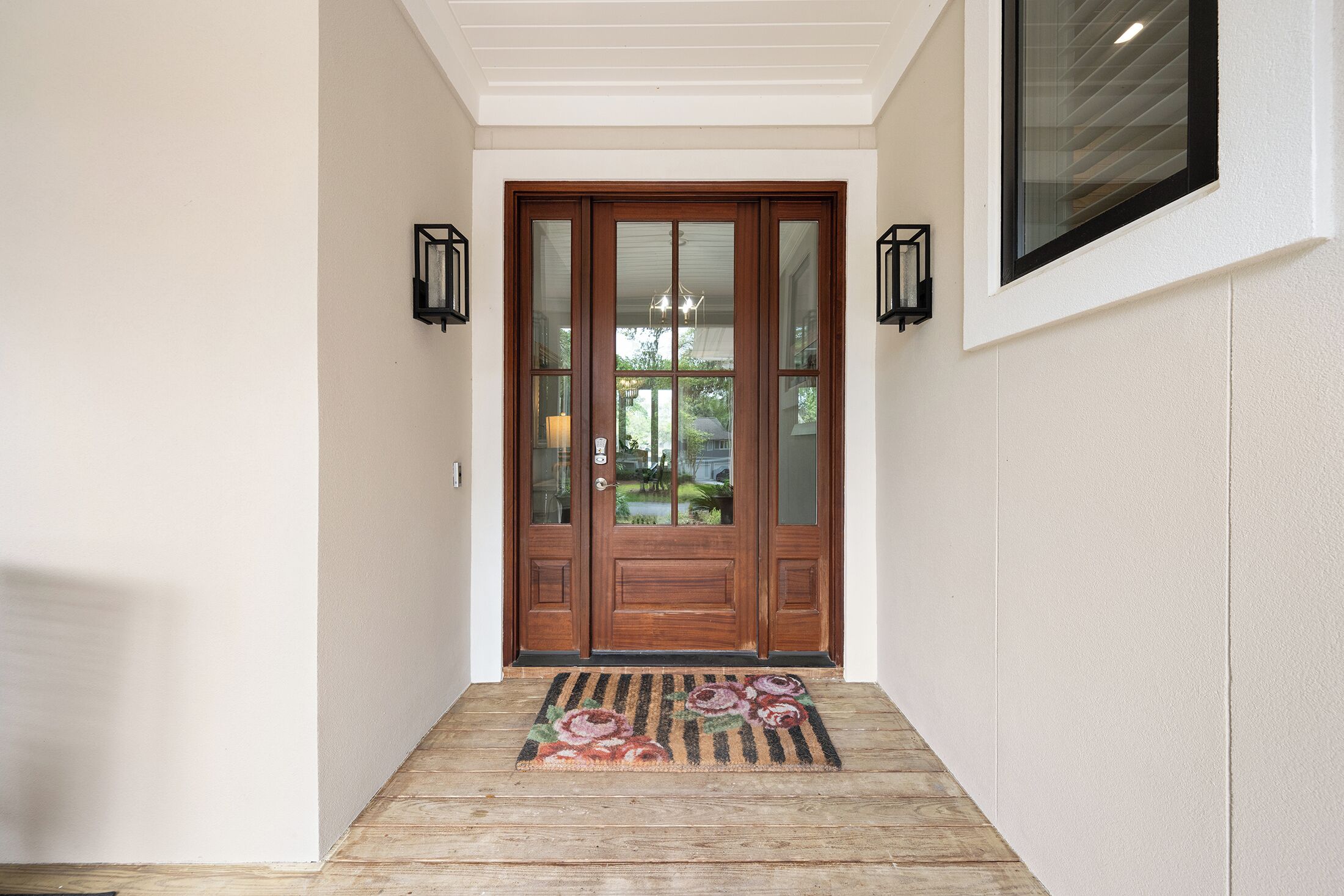 A wooden front door with glass panels, a doormat, and two wall-mounted lanterns.
