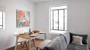 A modern living room with a grey sofa, a wooden dining table, and a colorful abstract painting on the wall. - A Modern and Homely 2BD Apartment in TLV (Tel Aviv)