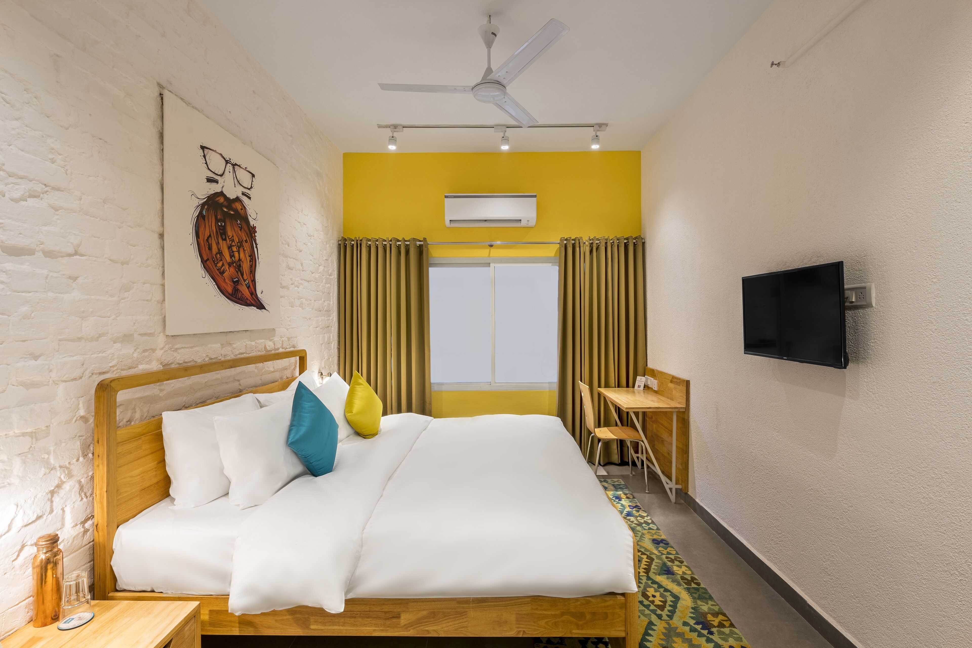 Una habitación de hotel con cama, escritorio, televisor y ventana con cortinas.