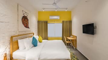 Una habitación de hotel con cama, escritorio, televisor y ventana con cortinas.