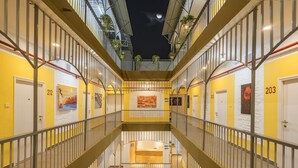 A multi-level hotel corridor with yellow walls, numbered doors, and a central staircase. - Bedzzz Varanasi by Leisure Hotels (Varanasi)
