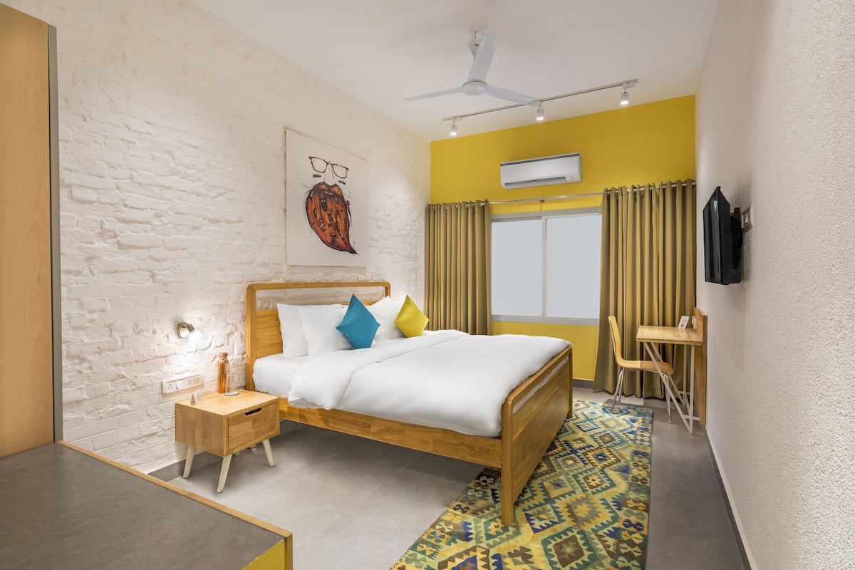 A modern bedroom with a wooden bed, a bedside table, a small desk, and a patterned rug.