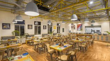 Un restaurante espacioso con techos altos, vigas a la vista e iluminación colgante. Las mesas están dispuestas de forma informal con sillas.