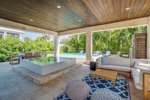 A covered outdoor area with a pool, seating, and a view of a residential building and palm trees.