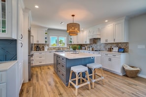 A modern kitchen with white cabinetry, a central island with stools, and a hanging light fixture.