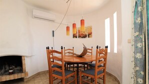 Uma sala de jantar com uma mesa redonda de madeira e seis cadeiras, uma lareira e um ar condicionado fixado na parede.