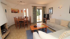 Uma sala de estar com lareira, um sofá, uma TV e um espaço de jantar com cadeiras e uma mesa.