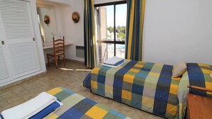 Quarto com cama, poltrona, escrivaninha e janela com cortinas.