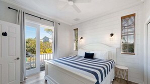 A bedroom with a bed, a ceiling fan, a window with blinds, and a door leading to a balcony. - Mango Bay – Luxury Island Home w/ Heated Pool, Spa & Walk To Beach (Holmes Beach)