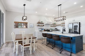 A modern kitchen with a central island, bar stools, and a dining table with chairs. - Mango Bay – Luxury Island Home w/ Heated Pool, Spa & Walk To Beach (Holmes Beach)