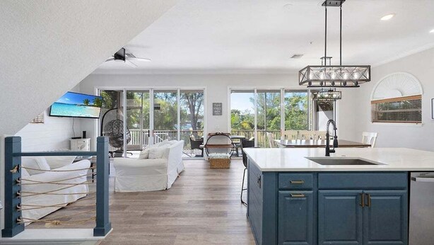 A spacious kitchen with a large island, a dining area with a table and chairs, and a cozy seating area with a sofa and a fan. - Mango Bay – Luxury Island Home w/ Heated Pool, Spa & Walk To Beach (Holmes Beach)